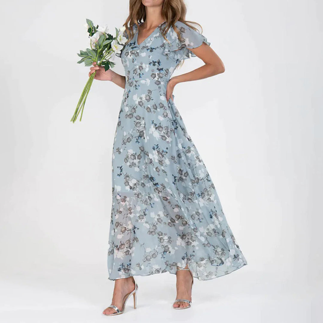 Frau in blauer, geblümter Maxikleid aus Chiffon, hält Blumenstrauß, elegante Sommermode.