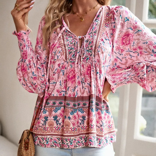 Frau trägt rosa Boho-Bluse mit Blumenmuster, lange Ärmel, V-Ausschnitt, lässiger Stil.