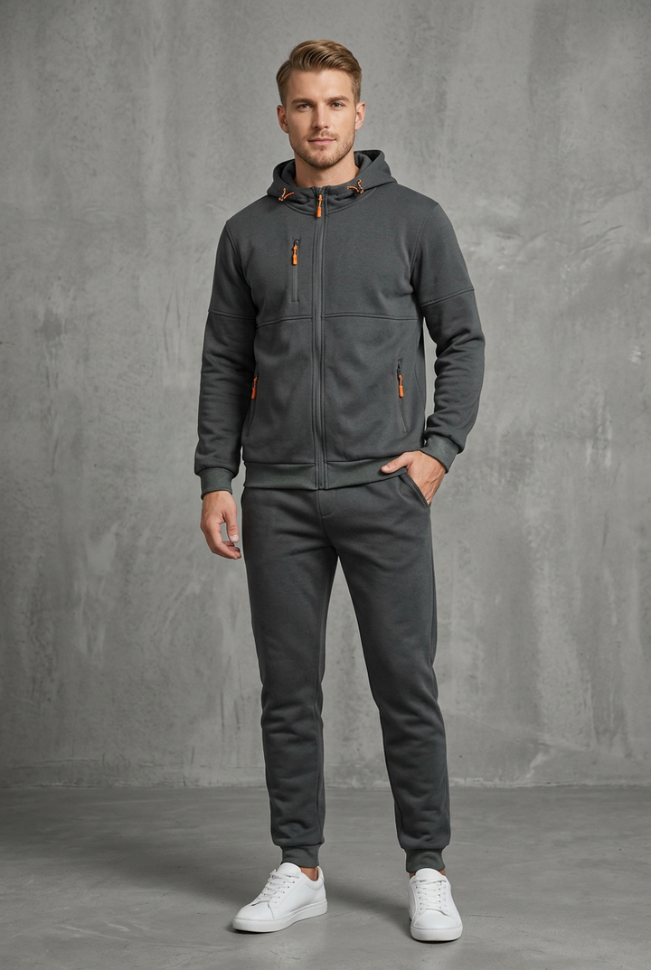 Front view of a dark charcoal gray zip hoodie and joggers with orange zipper pulls on a model 4