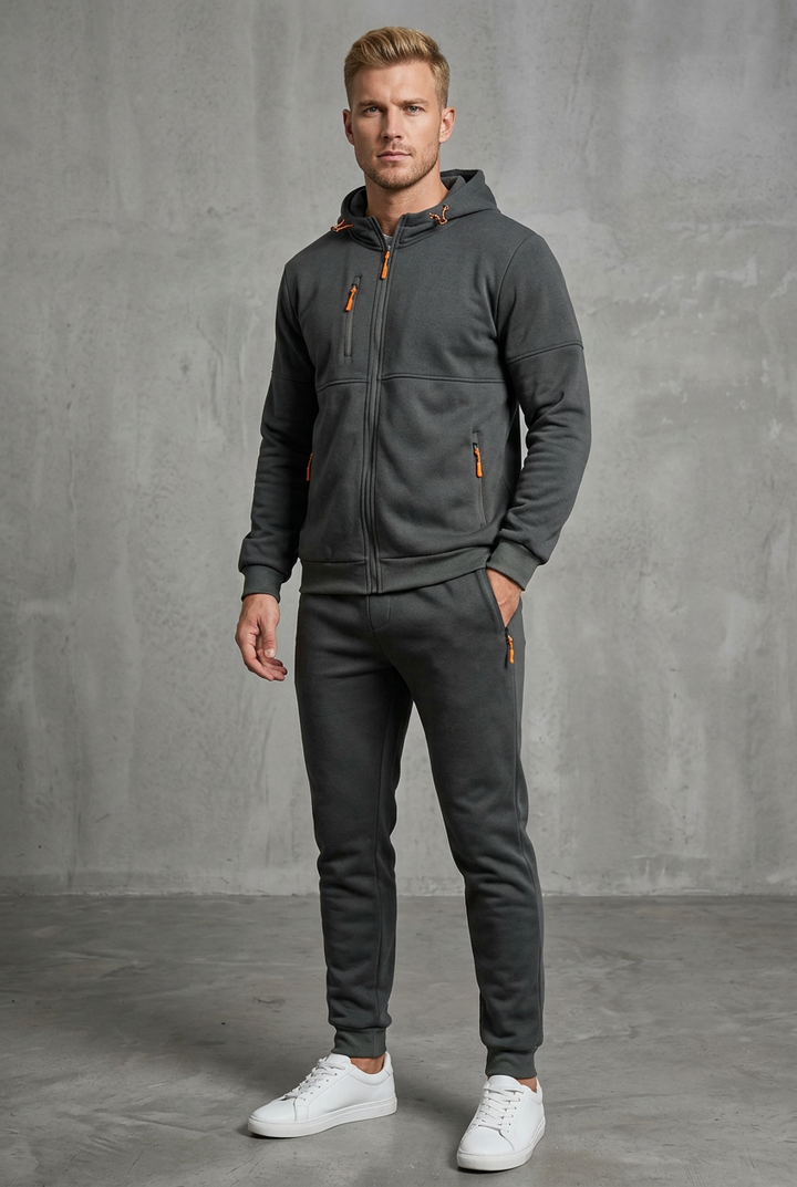 Man in dark charcoal gray hooded zip jacket and joggers with orange zipper pulls, hand in pocket 4