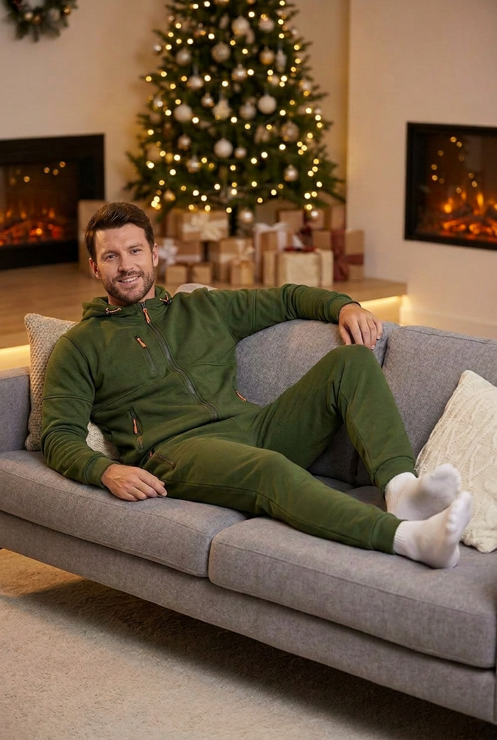 Smiling man in olive green zip hoodie and joggers relaxing on a gray sofa by a Christmas tree 1