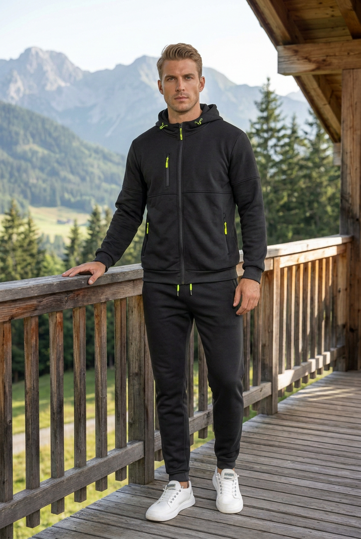 Man in black zip hoodie and joggers with neon yellow zipper pulls, standing on a mountain balcony 1