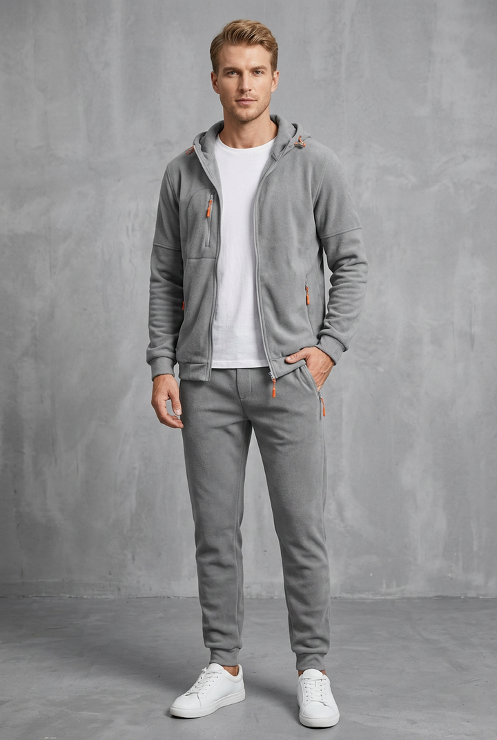 Front view of a light gray fleece zip hoodie and joggers with orange zipper pulls on a model 10
