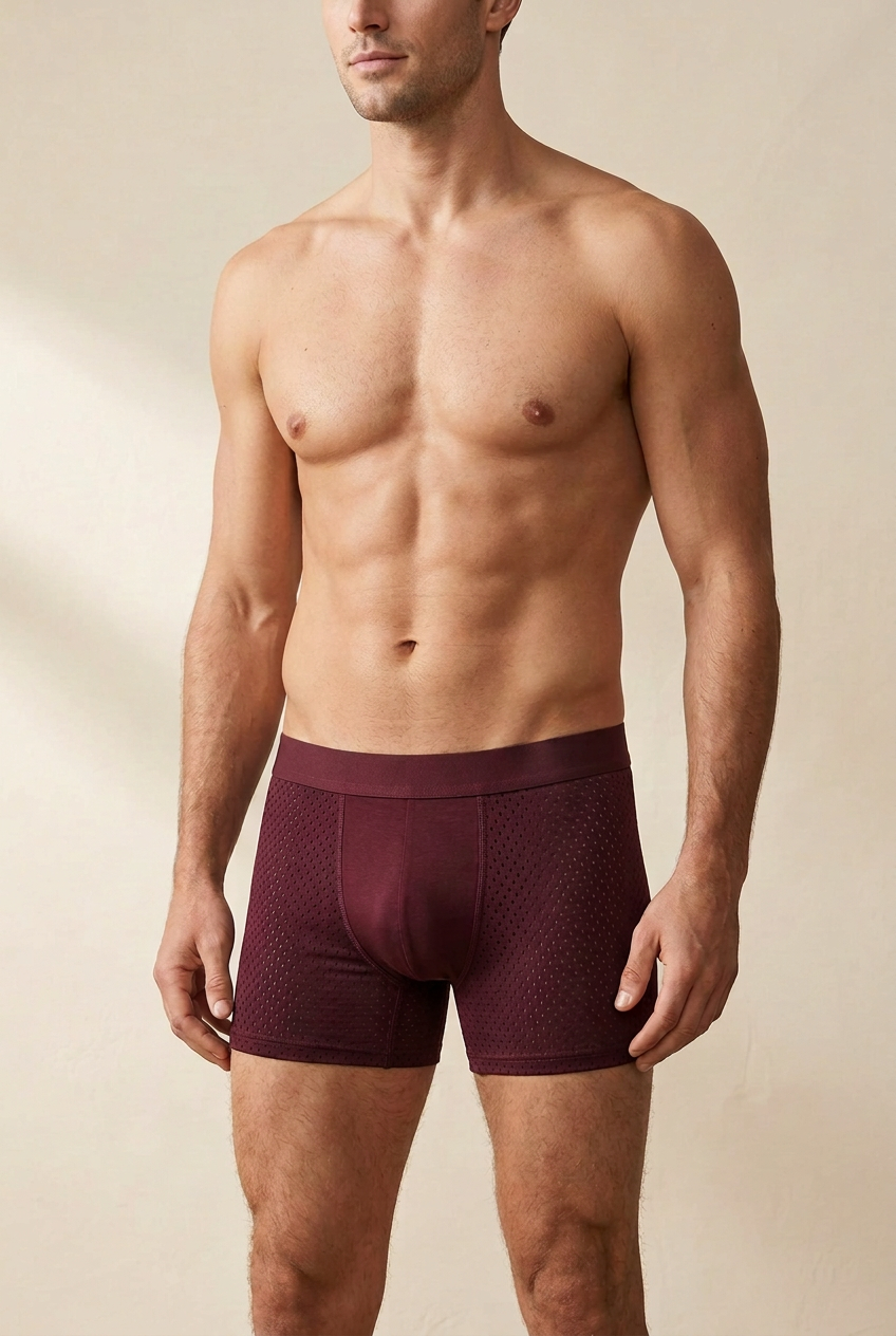 Shirtless male model wearing burgundy boxer briefs with perforated mesh side panels and a smooth center front 1