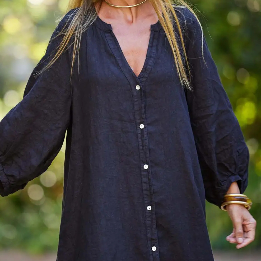 Frau in schwarzem Leinenkleid mit Knopfleiste, langen Ärmeln, draußen im Grünen.