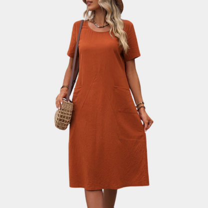 Frau in orangefarbenem Sommerkleid, Strohhut, Umhängetasche, lässiger Look.