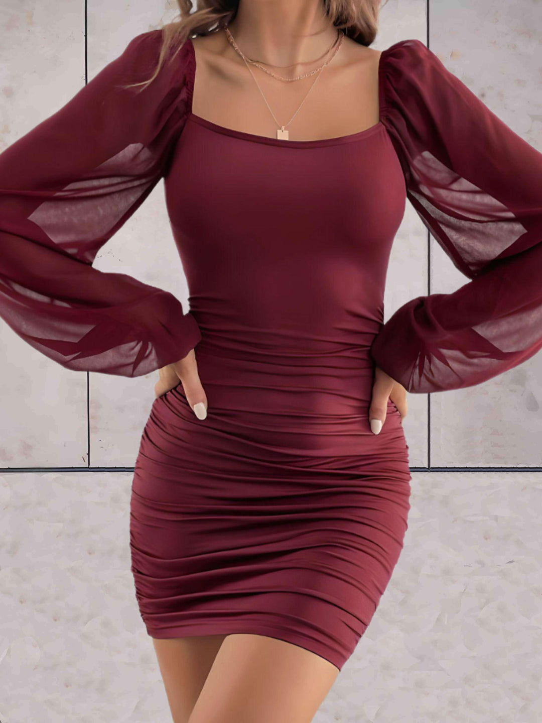 Frau in bordeauxfarbenem, figurbetontem Kleid mit langen, transparenten Ärmeln.