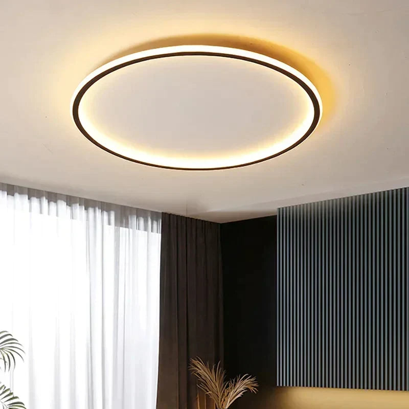 Black-framed round LED ceiling light lit warm in a room with sheer curtains and a dark wall 2