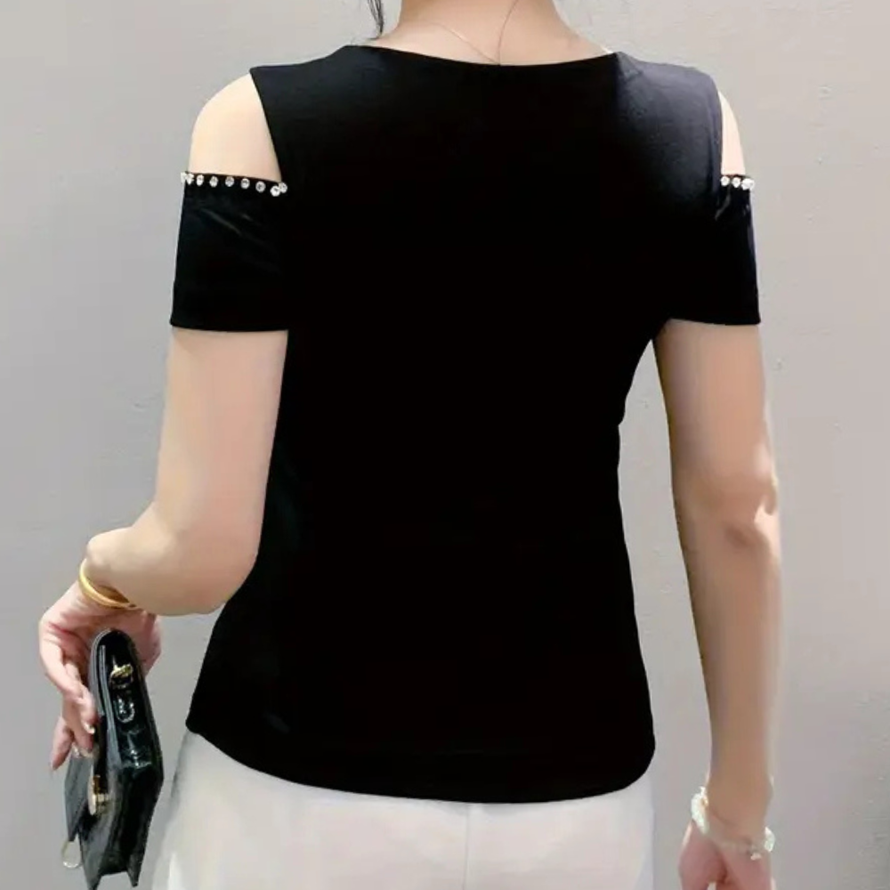 Frau in schwarzem, schulterfreiem Top mit Perlen, hält schwarze Clutch, modisch, elegant.