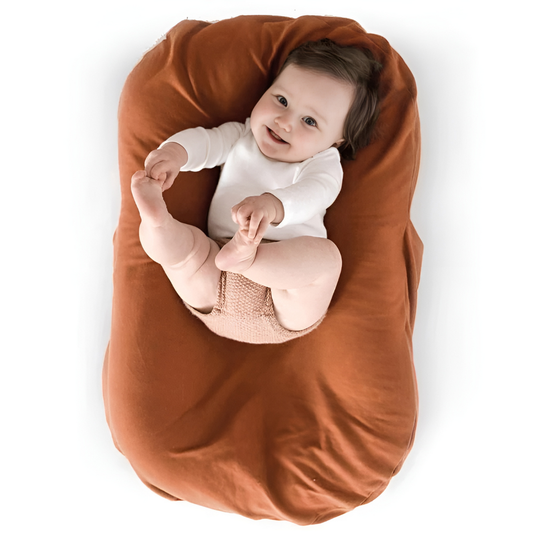 Baby in a white bodysuit holding both feet on a rust-orange lounger 6