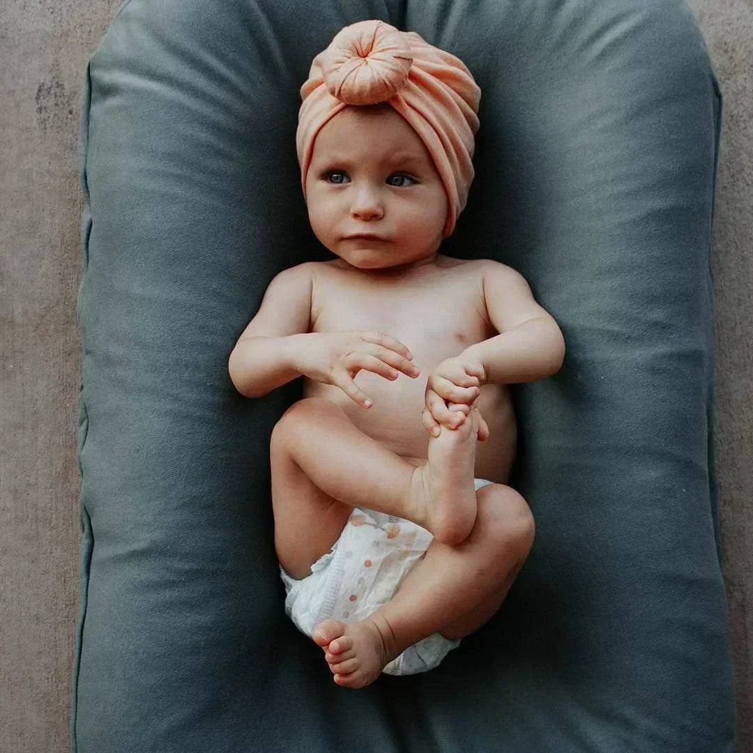 Baby in a peach knotted headwrap and diaper lying on a gray-blue lounger 2