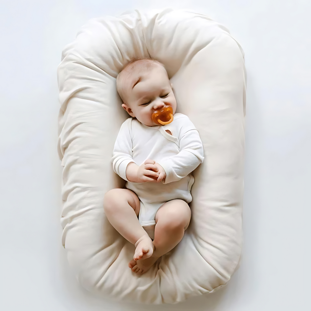 Sleeping baby with an amber pacifier lies in a cream lounger on a white background 6