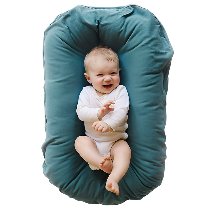 Laughing baby in a white bodysuit lies in a teal lounger, seen from above 2