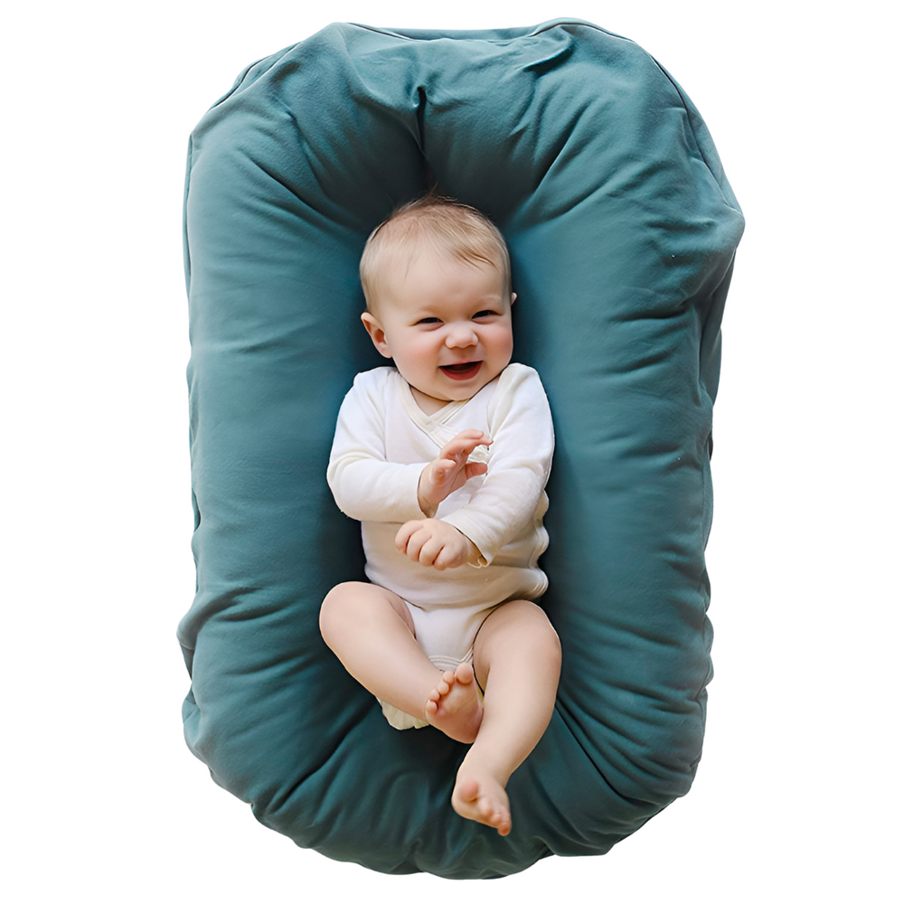 Top view of a laughing baby in a white bodysuit lying in a teal nest cushion 2