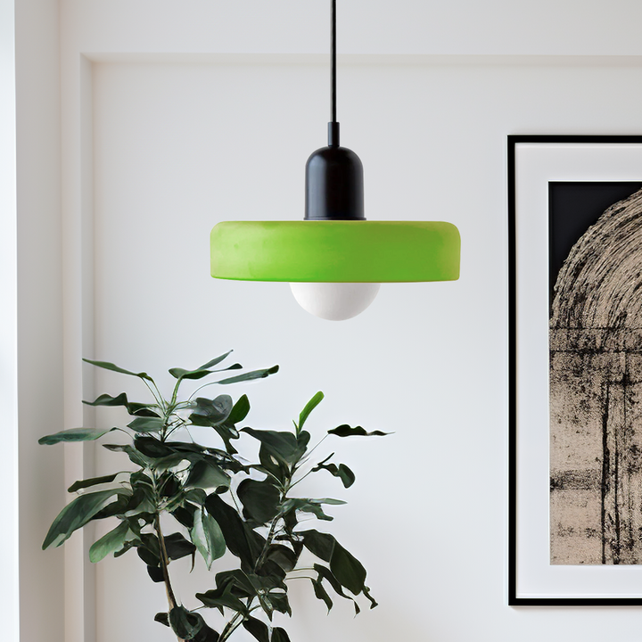 Lime-green disc pendant lamp with a black cap hanging beside a leafy plant and framed artwork 53