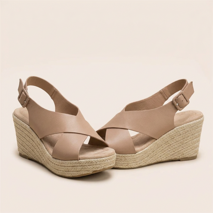 Pair of tan crisscross wedge sandals with buckled heel straps and cushioned footbeds on a cream background 13