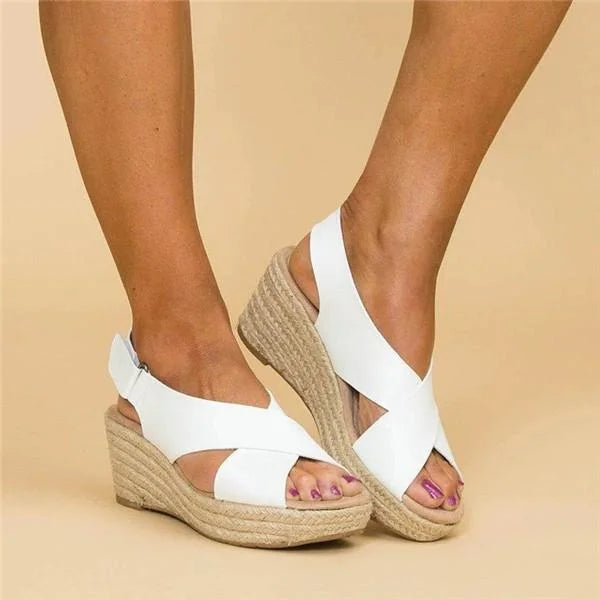 White crisscross wedge sandals worn on a beige background, one foot angled to show the ankle strap closure 6