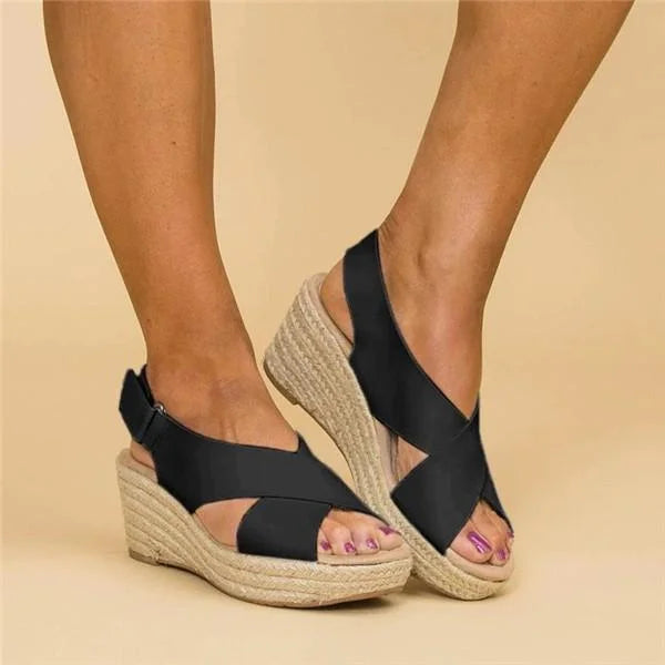 Black crisscross wedge sandals worn on feet, one foot turned to show the heel strap and woven wedge 7