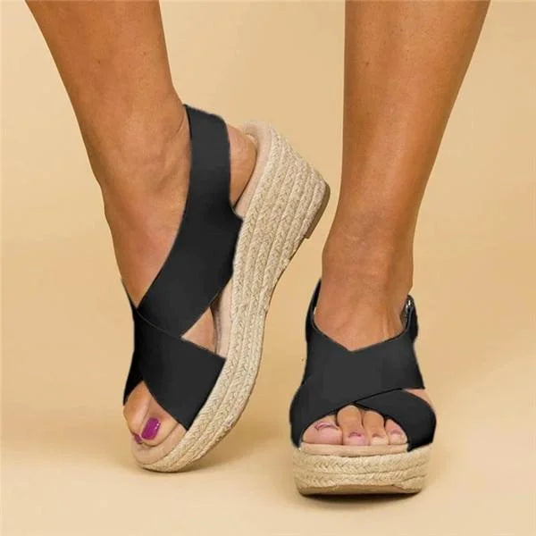 Black crisscross-strap wedge sandals worn on feet, viewed from the front and side against a beige backdrop 8