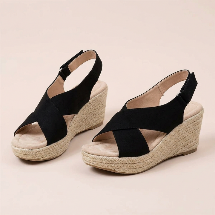 Pair of black crisscross wedge sandals on a blush background, showing padded footbeds and hook-and-loop heel straps 12