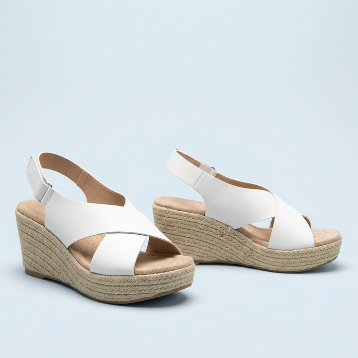 Pair of white crisscross wedge sandals with braided jute wedges photographed on a pale blue background 14