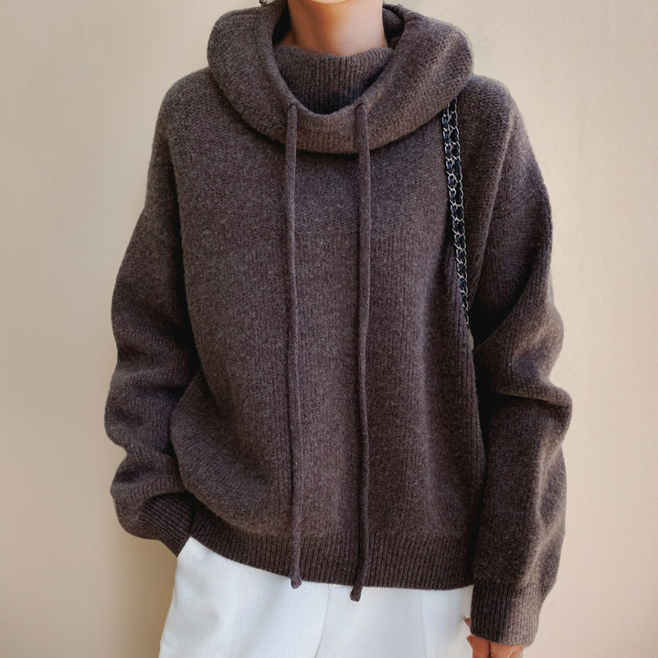 Front view of the brown knit sweater with centered drawstrings and ribbed hem, worn with white pants 8