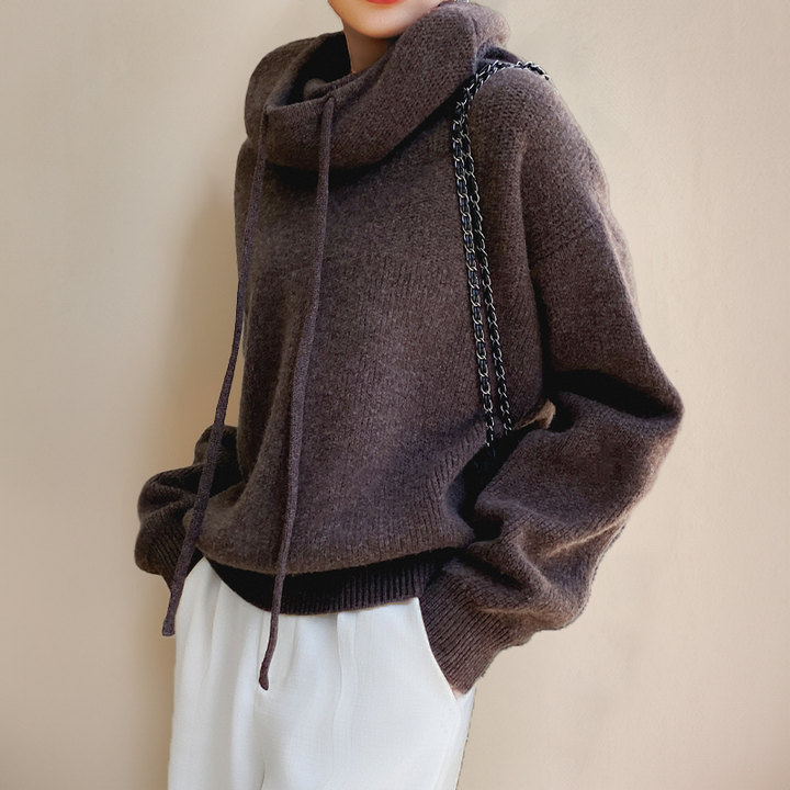 Brown hooded knit sweater with drawstrings, worn with white pants and a chain-strap bag 7