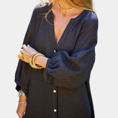 Frau in schwarzer Leinenbluse mit Knöpfen und langen Ärmeln, goldene Armreifen, modisch.