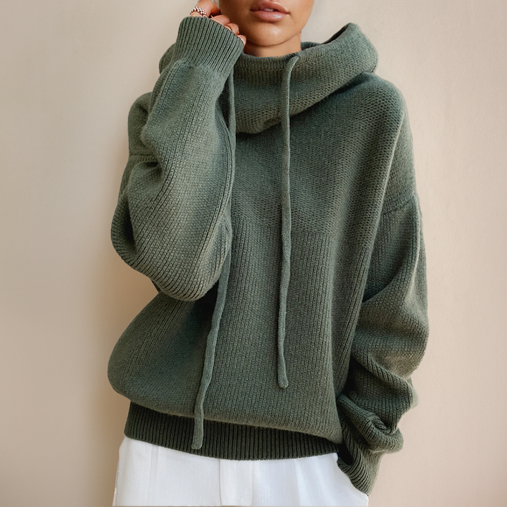 Green knit sweater with drawstring cowl hood, worn with white pants, shown cropped from chin to hips 2