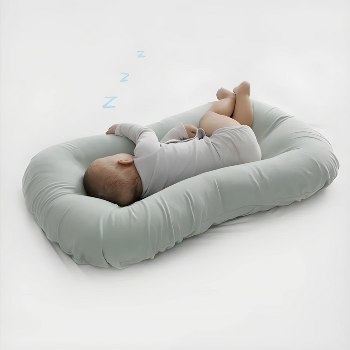 Baby sleeping on its side in a sage green cushion, with small z letters above 4
