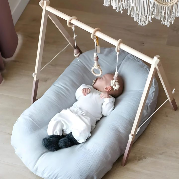 Baby lying on a light blue cushion beneath a wooden play gym with hanging rings 6