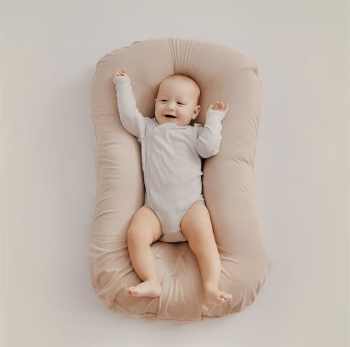 Overhead view of a happy baby with raised arms on a beige soft pillow 7