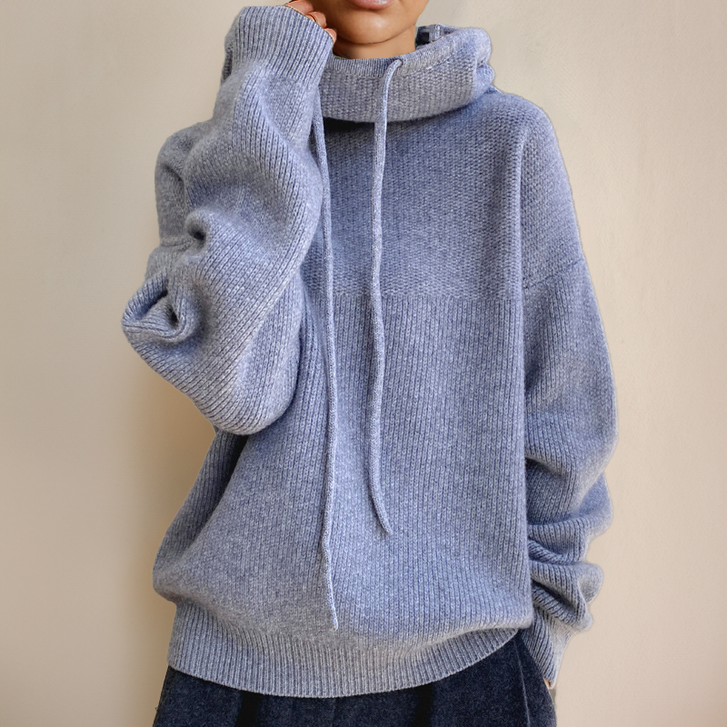 Blue-gray sweater with an oversized fit, long drawstrings and dark trousers, one hand at the neck 6
