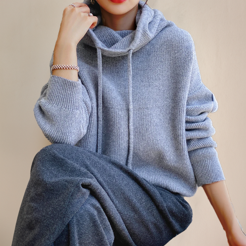 Woman sitting in a light gray ribbed knit sweater with a drawstring cowl hood, hand raised near her face 5