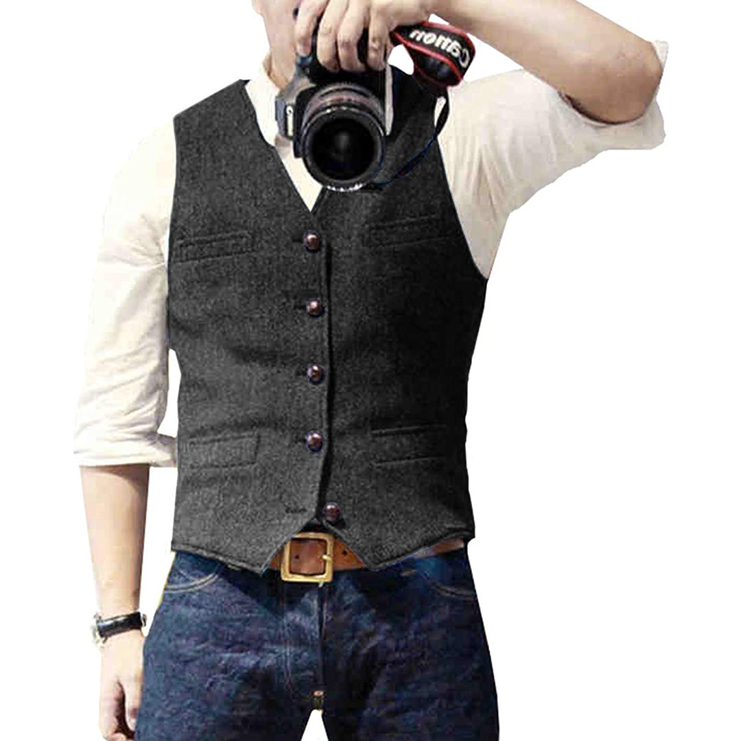 Mann mit grauem Wollweste, weißem Hemd, Jeans, hält Kamera.
