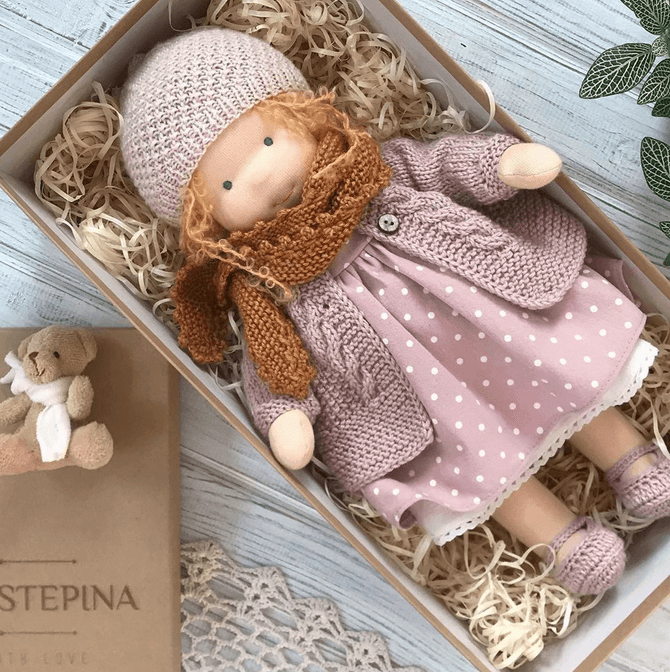 Top view of doll with auburn curls, pink dotted dress, knit cardigan and rust scarf in a box on straw 5