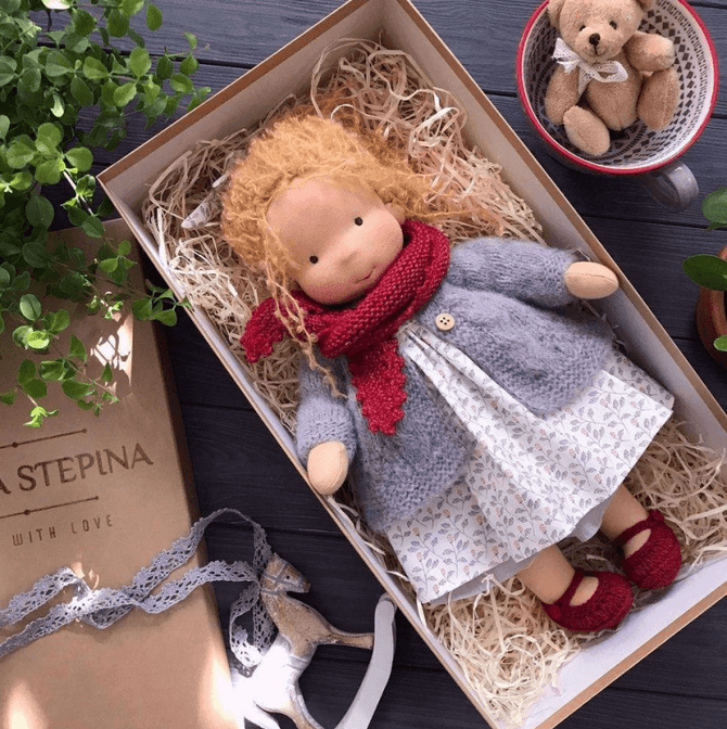 Ginger-haired doll in a gray cardigan, red scarf and red shoes, lying in a straw-filled box with a teddy in a cup 9