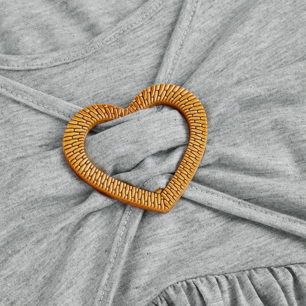 Herzförmige, goldene Brosche auf grauem Stoff, Schmuckaccessoire, elegant, modisch.