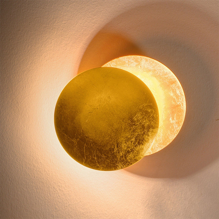 Close-up of the gold-leaf front disc overlapping a softly lit back disc on a textured wall 11