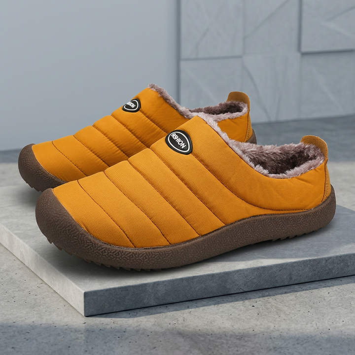 Mustard orange quilted slippers on a gray platform, showing the padded ridges and brown sole 20