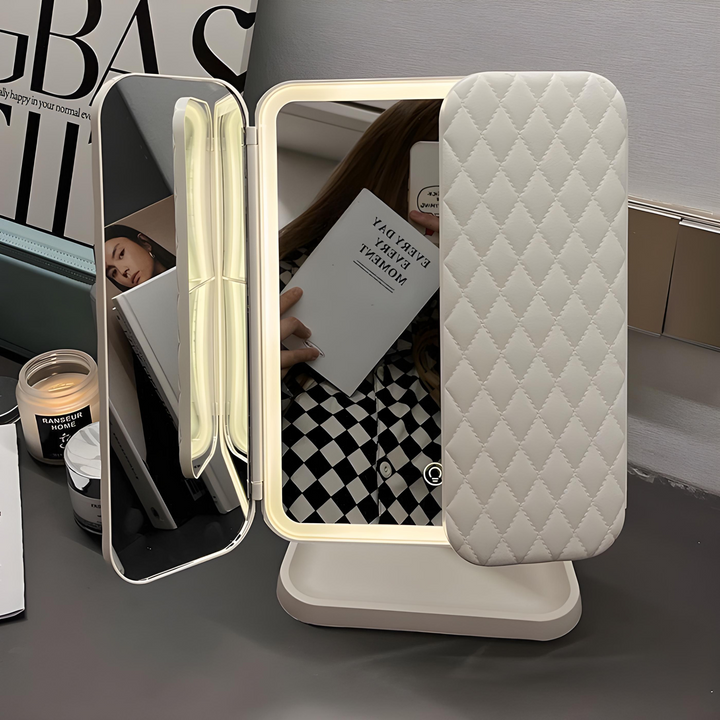 Cream tri-fold mirror with glowing LED frame on a desk, one panel folded in quilted cover 1