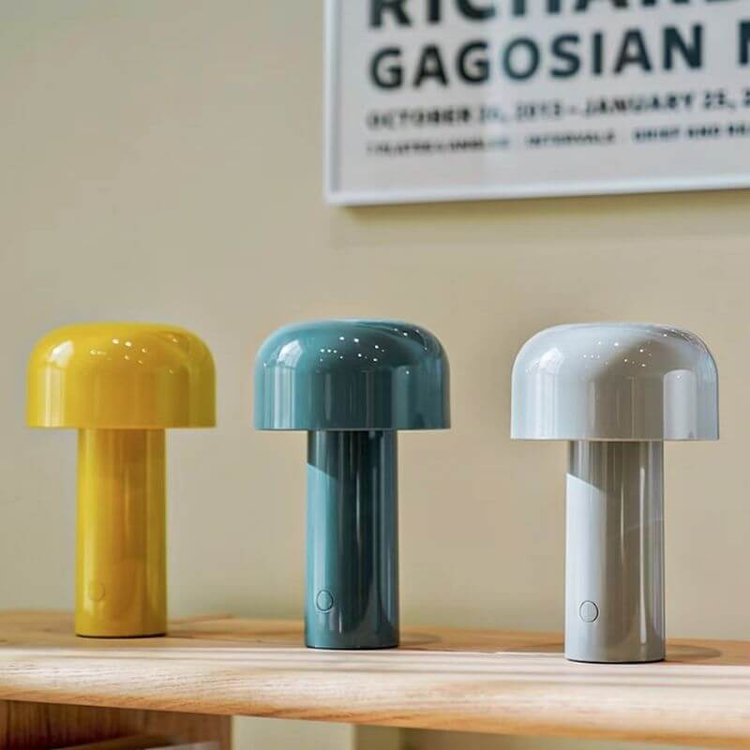 Yellow, blue and gray mushroom lamps lined up on a wooden shelf beneath a framed poster 10