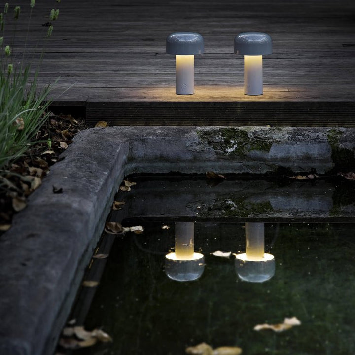 Two lit lamps on a wooden deck, their glow reflected in a dark pond below 13