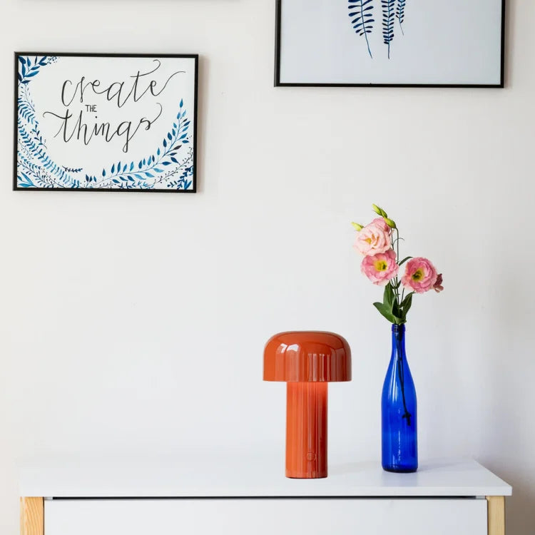 Orange lamp on a white dresser next to a blue vase with pink flowers and framed prints 20