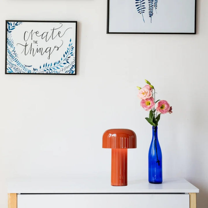 Orange mushroom lamp on a white dresser beside a blue bottle holding pink flowers 20