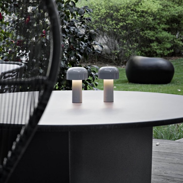 Pair of gray mushroom lamps lit on a round outdoor table with a garden behind 23