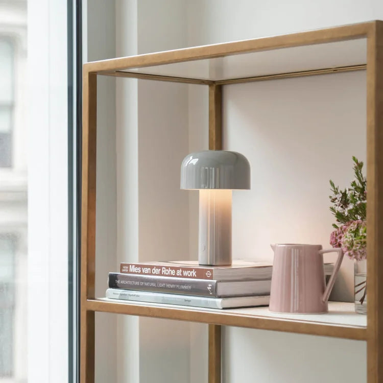 Gray mushroom lamp glowing on a shelf with stacked books, a pink pitcher and flowers 23