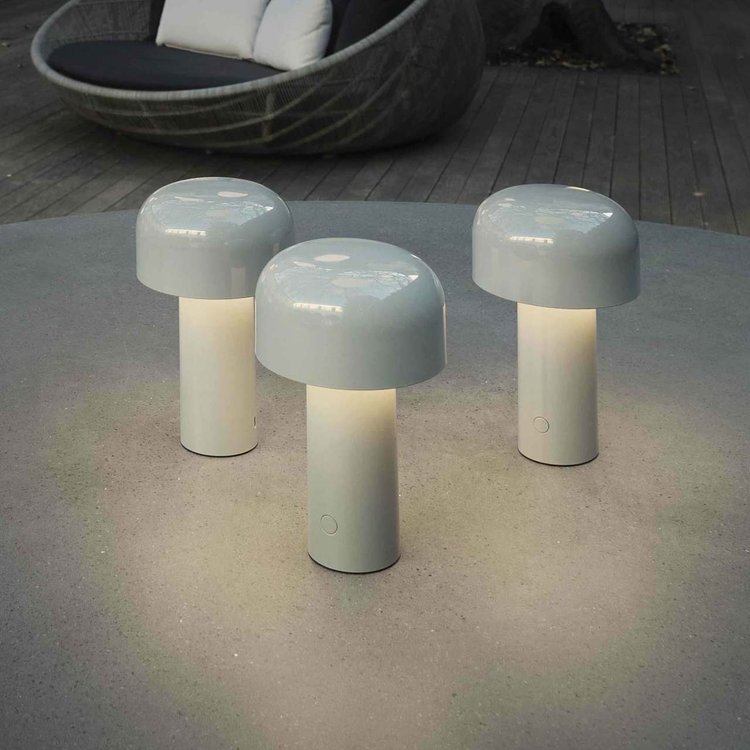 Three light gray lamps glowing warmly on a round concrete outdoor table near a wicker lounger 7