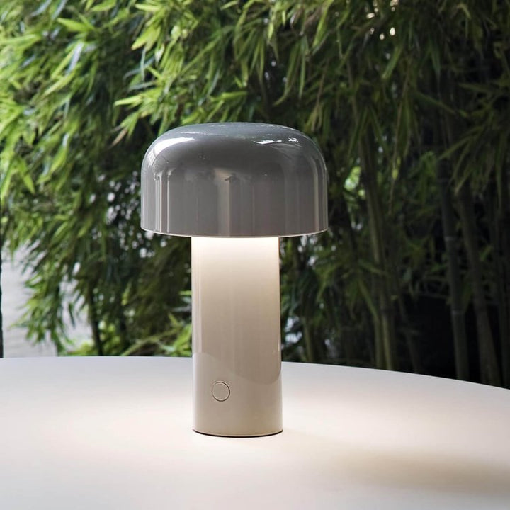 Lit gray mushroom lamp on a white round table in front of green bamboo 9