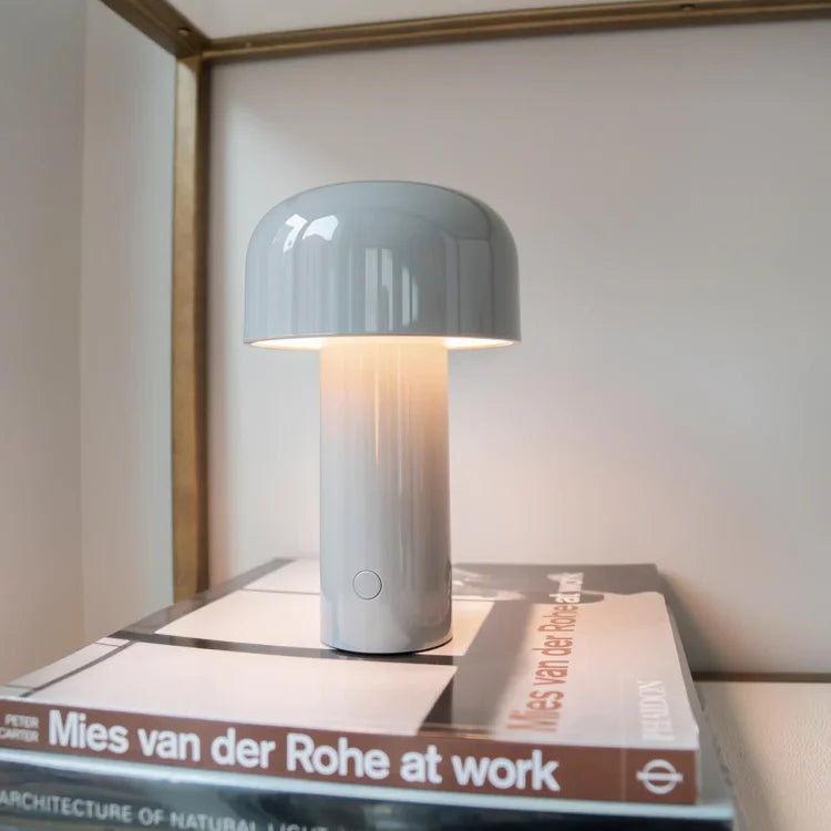 Light gray lamp glowing on a stack of art books in front of a pale wall 10